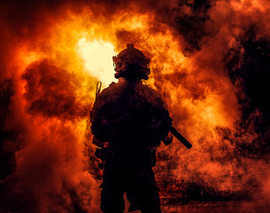 Silhouette of modern infantry soldier, elite army fighter in tactical ammunition and helmet, standing with assault service rifle in hands on background of fiery explode. Burning fire of war conflict