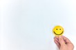 A hand holding a yellow happy face in white background with copy space. Positive customer feedback and review. Happiness and Good service concept.