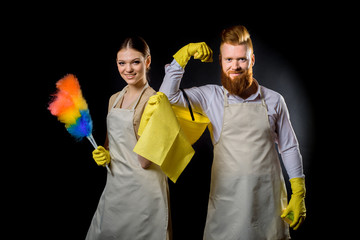 House cleaning. Duty and cleaner on black n the studio. In yellow gloves with a yellow sponge, a spray and a bucket. A red-bearded man and beautiful girl in military uniform and uniform