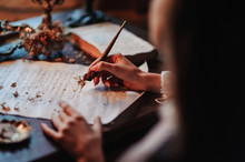 Girl Writes A Letter With An Antique Fountain Pen. A Female Hand Holds A Pen Over A Sheet Of Paper In The Light Of A Candle.