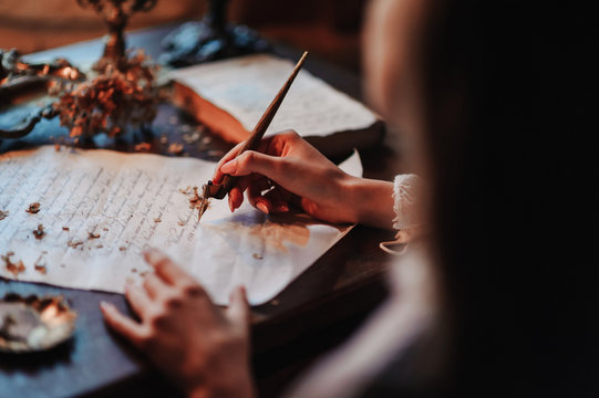 Girl writes a letter with an antique fountain pen. A female hand holds a pen over a sheet of paper in the light of a candle.
