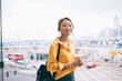© BullRun - Smiling Asian young woman holding coffee on panoramic window background