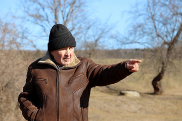 Elderly man pointing out something on a spring forest background. Concept of life in village, vision in old age