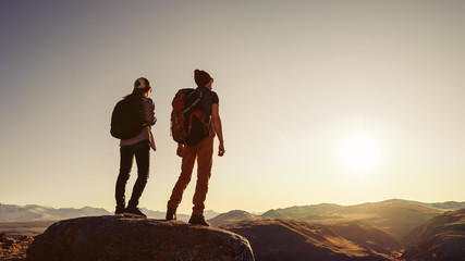 Wall Mural - two travelers stands at sunset rock in mountains