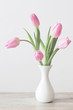 pink tulips in white ceramic vase on wooden table on background white wall