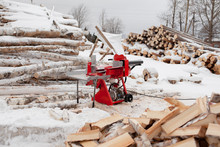 Red Woodcutter Stands In The Middle Of Split Logs In Winter Next To The Production