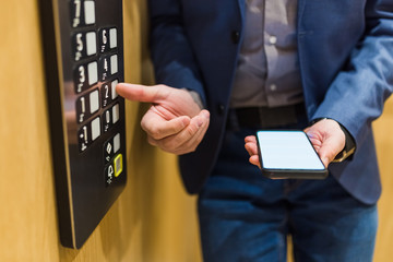 Close up of businessman using blank screen smartphone and pressing elevator button. Business and office building meeting concept.