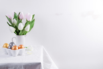 Wall Mural - Golden Easter Eggs in ceramic egg tray with tulip on white table. Easter background or easter concept.