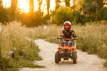 The Little Girl Rides A Quad Bike ATV. A Mini Quad Bike Is A Cool Girl In A Helmet And Protective Clothing. Electric Quad Bike Electric Car For Children Popularizes Green Technology.