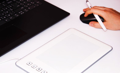 Female hands work on a graphic tablet. Hand holds stylus pen and draws. White graphic tablet. The work of a graphic designer. Girl works on a tablet connected to a laptop. Rear view from  behind