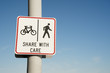 © Chameleon Pictures - share with care warning sign on a shared path for pedestrians and cyclists against a clear blue sky background