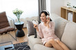 © Blue Jean Images - Happy young Chinese woman wearing headphones on sofa