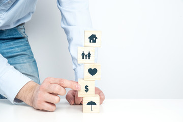 Poster - Insurance symbols on wooden blocks. Insurance and security concept. Health, life and valuable items insurance. Securing the family. The man is arranging the money.