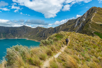 Young male backpacker walking along the magic Quilotoa crater lake on the hike named Quilotoa Loop in the Andes mountain range near Quito, Ecuador.