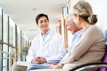 Wall Mural - young asian doctor talking to senior couple patients in hospital hallway