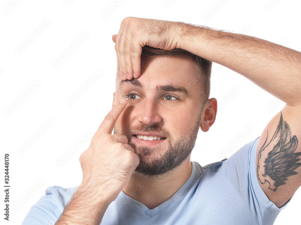 Young man putting in contact lenses on white background