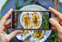Woman Take Picture Of Food With Phone. Smartphone Lunch Photo Of Baked Stuffed Potato In The Kitchen. Vegan Healthy Diet Food. Lifestyle Trendy Social Media Style.