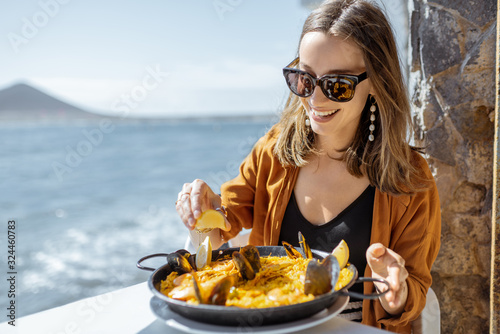 Fotografía Woman eating paella, traditional spanish dish, while sitting at the restaurant terrace near the ocean