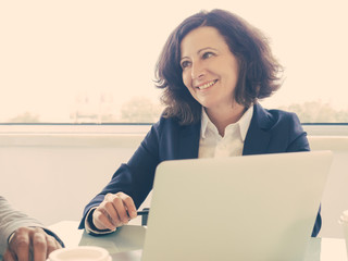 Wall Mural - Happy successful female manager discussing deal with partners. Business woman sitting at meeting table, looking away and speaking. Professional at meeting concept