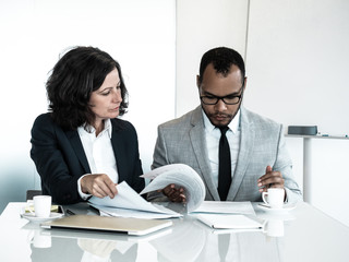 Wall Mural - Business colleagues checking agreement text. Business man and woman sitting at meeting table and reading documents together. Teamwork concept