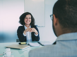 Wall Mural - Personnel manager interviewing male candidate. Business man and happy woman sitting at meeting table opposite of each other. Job meeting concept