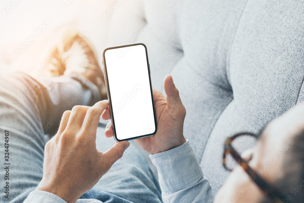 Mockup image blank white screen cell phone.man hand holding texting using mobile on sofa at home.background empty space for advertise text.people contact marketing business,technology - obrazy, fototapety, plakaty 