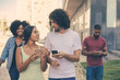 © Mangostar - Beautiful young couple with smartphones excited with discussion outdoors. Mix raced man with mobile phone and black woman walking behind them. Communication outdoors concept