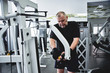 © amixstudio - Adult gray-haired man trains on fitness equipment in the gym, pumps legs and arms muscles, loses weight. Concept of healthy lifestyle in old age