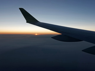 Sunset from a plain. View through the window of an aircraft. Wing of the plane above clouds