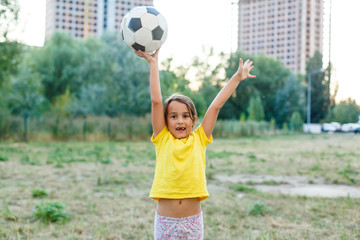 Outdoor photo of cute little girl leaning on soccer ball in green grass