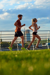 Modern woman and man jogging / exercising in urban surroundings near the river.