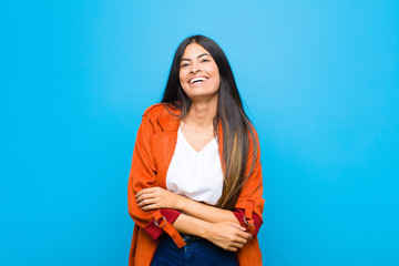 Wall Mural - young pretty latin woman looking like a happy, proud and satisfied achiever smiling with arms crossed against flat wall