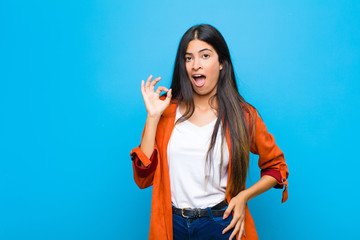 Wall Mural - young pretty latin woman feeling successful and satisfied, smiling with mouth wide open, making okay sign with hand against flat wall