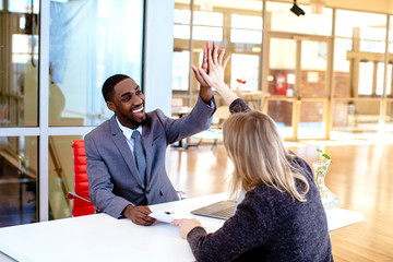 Portrait of a happy smiling young man in business suit celebrating while giving a high five to woman coworker or client in meeting