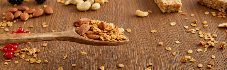 Wall Mural - Wooden spatula with granola above table and nuts, oat flakes and berries on wooden background, panoramic shot