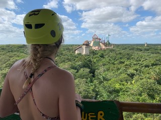 young lady is in adventure park in mexico.she is wearing a helmet for zip line. lush jungles are aro