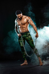 Wall Mural - Athlete bodybuilder on black background with lights and smoke. Men fashion. Portrait of a brutal bearded man topless with chains.