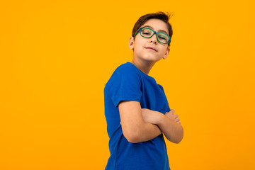 Wall Mural - cool teenager boy in a blue tank top and glasses with arms crossed on a yellow background with copy space