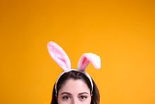 Studio Portrait Of Young Beautiful Woman Wearing Traditional Bunny Ears Headband For Easter And Smiling. Brunette Female With Wavy Hair Over Yellow Background. Close Up, Copy Space.