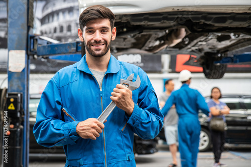 Fotomural Mechanic standing and hold a wrench with blur his assistant talking with customers in the background