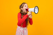© Ivan Traimak - teenager girl screaming news in a loudspeaker and stands sideways on a yellow studio background with copy space