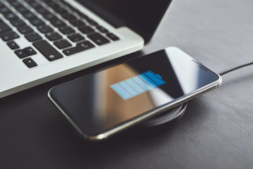Wall Mural - close up of wireless charging mobile phone on table next to laptop