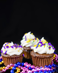 Three miniature cupcakes on a black background with colorful beads.  Copy space above.