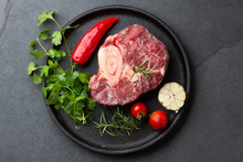 Raw Fresh Ossobuco Con Herbs, Garlic And Chile Pepper On Black Plate. Dark Background