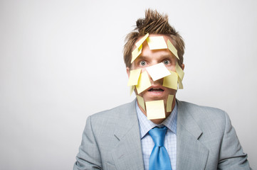 Confused businessman looking at the camera with yellow sticky notes covering his face