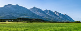 Fototapeta Do pokoju - Panoramic view at five of Seven Sisters Mountain range on Sandnessjoen, ideally green grass, small Norwegian village and mountains beside the field. Shinny sunny day, blue skies, Norway, copy space