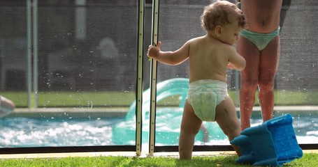 Wall Mural - Family at the swimming pool, infant baby in foreground and kids in background playing inside water