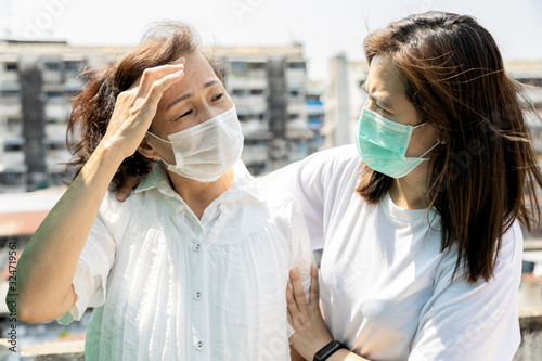 Tired asian senior woman has headache,elderly people wearing medical mask,touching aching head,feel sick,pain,attack of headache,illness from fine dust,PM2.5,air pollution,inhaling toxic fumes,smog