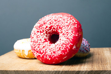 deliciously tasty red donut with white powder on a wooden stand on a gray background. closeup