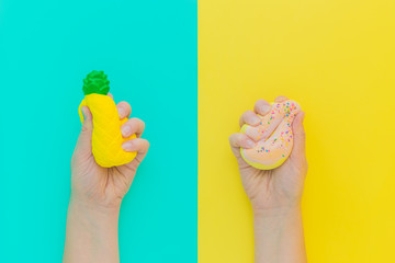 Flat lay antistress squish toys yellow pineapple,pink donut with sprinkles in hands.Bright blue background.Compressing,soft,squeezable items to relieve stress,problem,anxieties,worries.Summer concept